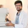 Optometrist looking up from eye test machine and smiling at camera