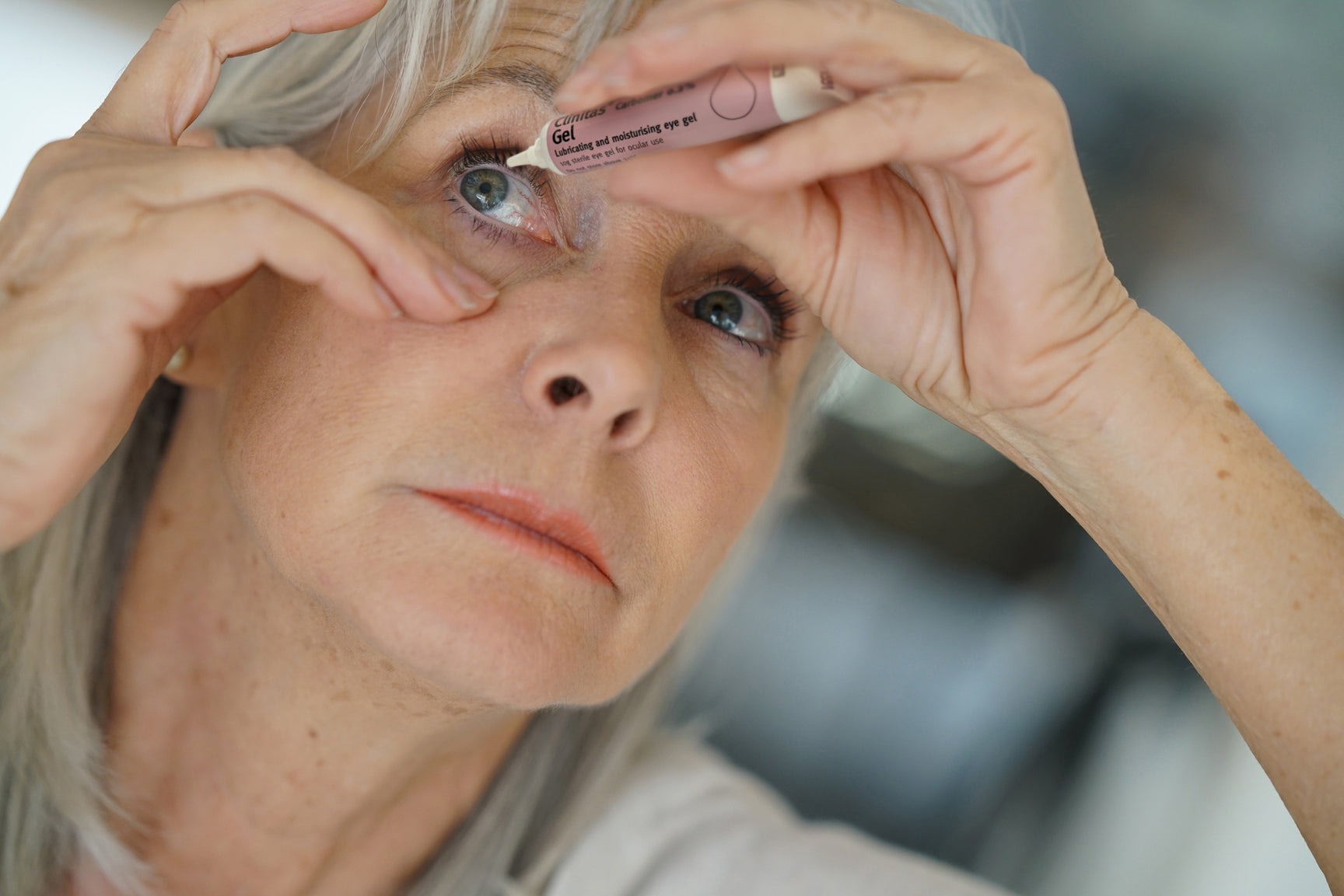 Older 60+ lady applying Clinitas hydrated carbomer gel to relieve her dry eyes